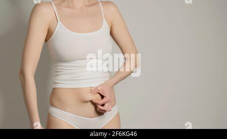 Skinny Fat Figur unkenntlich Frau quetscht ihren Bauch Fett. Frau`s Figur Nahaufnahme RAW Studio in grauem Hintergrund aufgenommen. Diät und Fettabbau conce Stockfoto